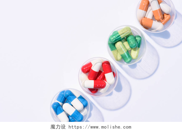 白色桌子上的四种不同的胶囊在白色的一排塑料碗中的各种彩色药丸的顶部视图